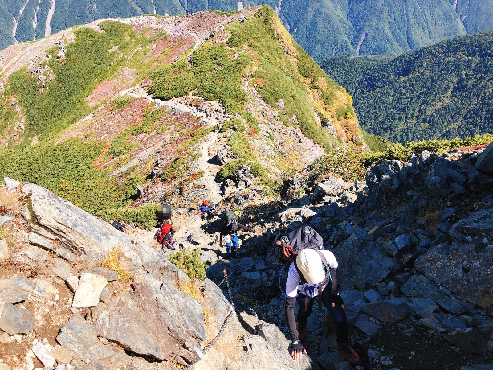北岳肩の小屋手前の岩場を登る登山者と草紅葉の稜線 北岳