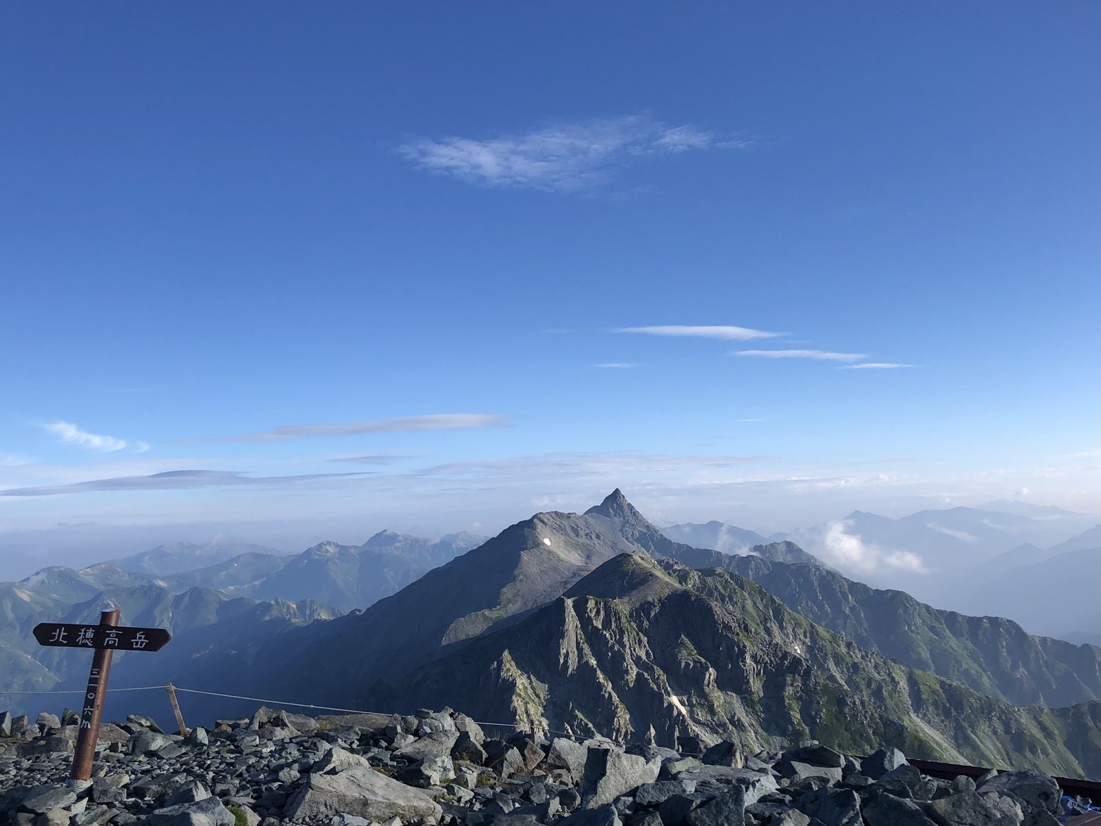 快晴の北穂高岳山頂標識と大キレットの先に立つ槍ヶ岳 北アルプス