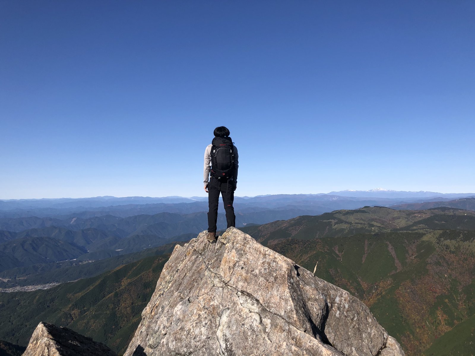 兜岩のとがった岩の先端に立ち大展望を眺める登山者 小秀山